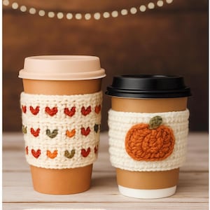 May include: Two coffee cups with cream-coloured crochet sleeves. One sleeve has a pattern of red, orange, and green hearts. The other has an orange pumpkin applique. The text "2 in 1 Pattern!" is at the bottom.