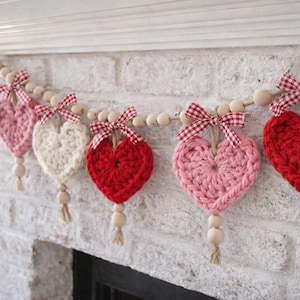 Peut inclure: Une guirlande de cœurs faite à la main avec cinq cœurs crochetés roses et rouges, enfilés sur une guirlande de perles en bois. Chaque cœur est orné d'un nœud vichy et d'un pompon en jute, parfait pour la décoration de la Saint-Valentin.
