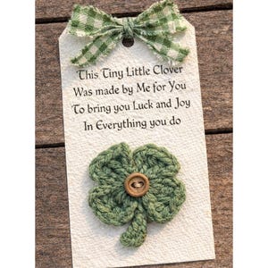 Puede incluir: Una etiqueta de regalo hecha a mano con un lazo verde a cuadros y un trébol de cuatro hojas tejido a ganchillo. La etiqueta dice: "This Tiny Little Clover Was made by Me for You To bring you Luck and Joy In Everything you do."