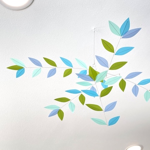 May include: A decorative mobile featuring paper leaves in shades of green, blue, and lavender. The leaves are attached to thin wires, creating a delicate, airy design. The mobile is suspended from the ceiling, adding a touch of nature-inspired decor.
