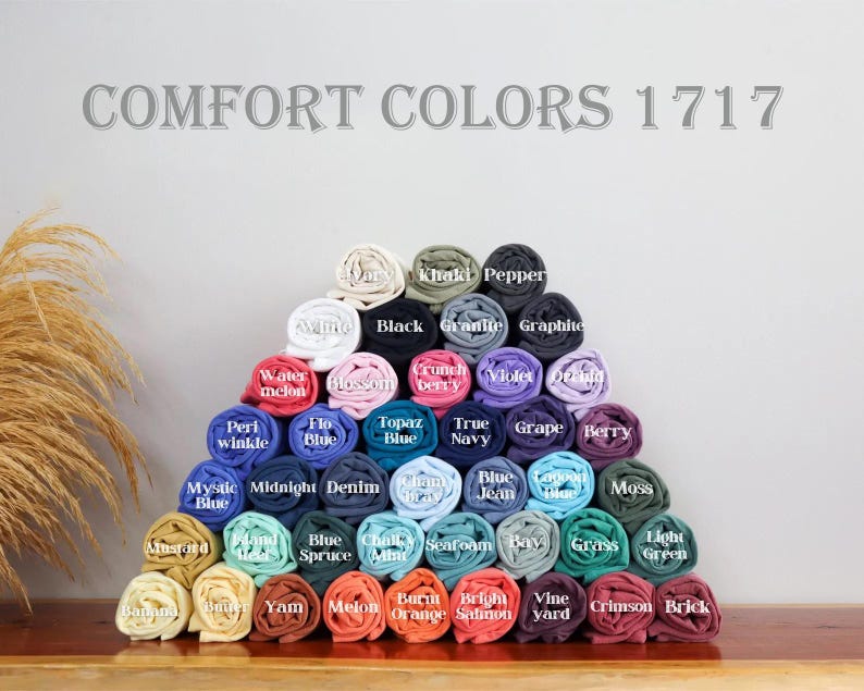 May include: A display of rolled t-shirts in various colors, arranged in a pyramid shape. The image includes the text "COMFORT COLORS 1717" at the top. Colors include black, blue, green, and red.