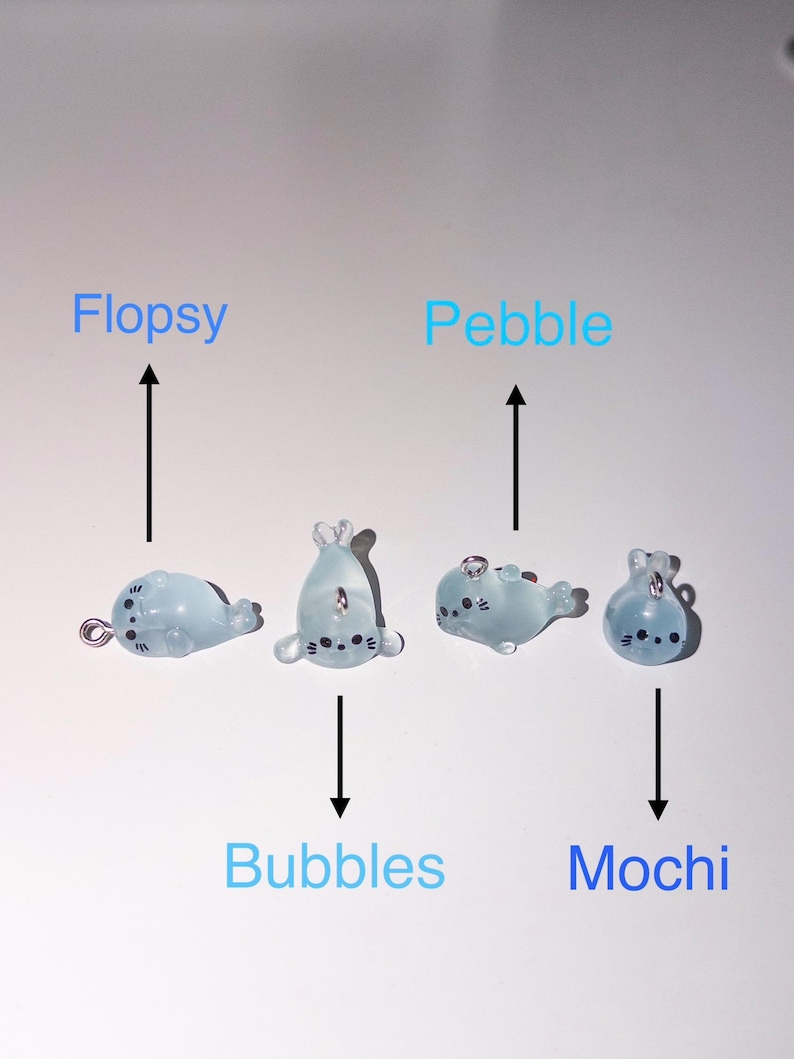 Peut inclure: Quatre breloques en forme de phoque bleu clair translucide avec des yeux et des moustaches peints en noir. Chaque breloque comporte une petite boucle m&eacute;tallique sur le dessus ou sur le c&ocirc;t&eacute;. Les noms Flopsy, Bubbles, Pebble et Mochi sont indiqu&eacute;s par des fl&egrave;ches noires pointant vers chaque figurine.