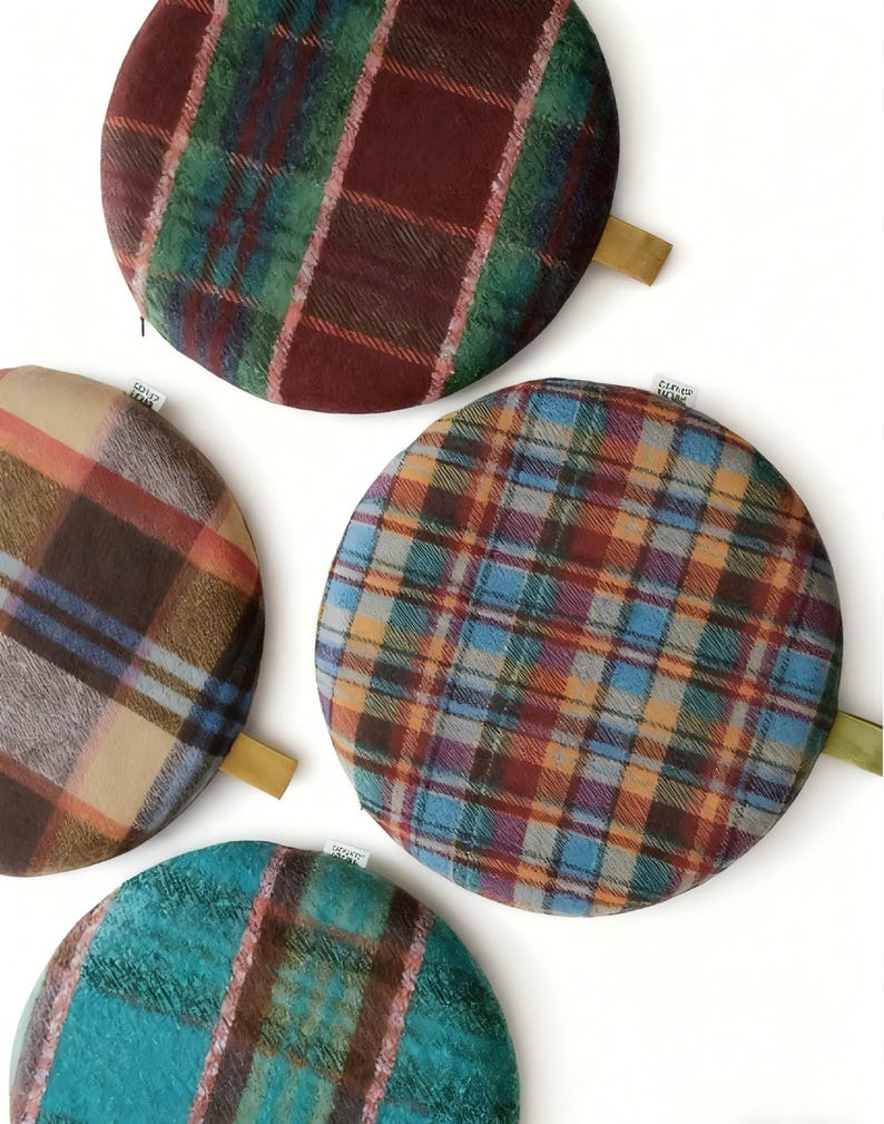 May include: A collection of round, plaid fabric items in various colors. The patterns include shades of red, green, blue, brown, and tan. Each item has a small, attached fabric loop. The items are arranged on a white background.