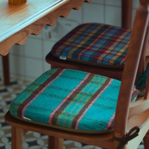 Puede incluir: Sillas de madera con cojines de asiento a cuadros. Un cojín es de color turquesa con rayas rosas y marrones, el otro es un estampado de cuadros multicolores. Una mesa de madera con borde festoneado y una taza amarilla en el fondo.