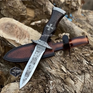 May include: A decorative dagger with a silver blade and a dark brown handle featuring a cross design. The dagger is in a brown leather sheath. The handle has intricate carvings and a silver cross. The sheath is embossed with a pattern.