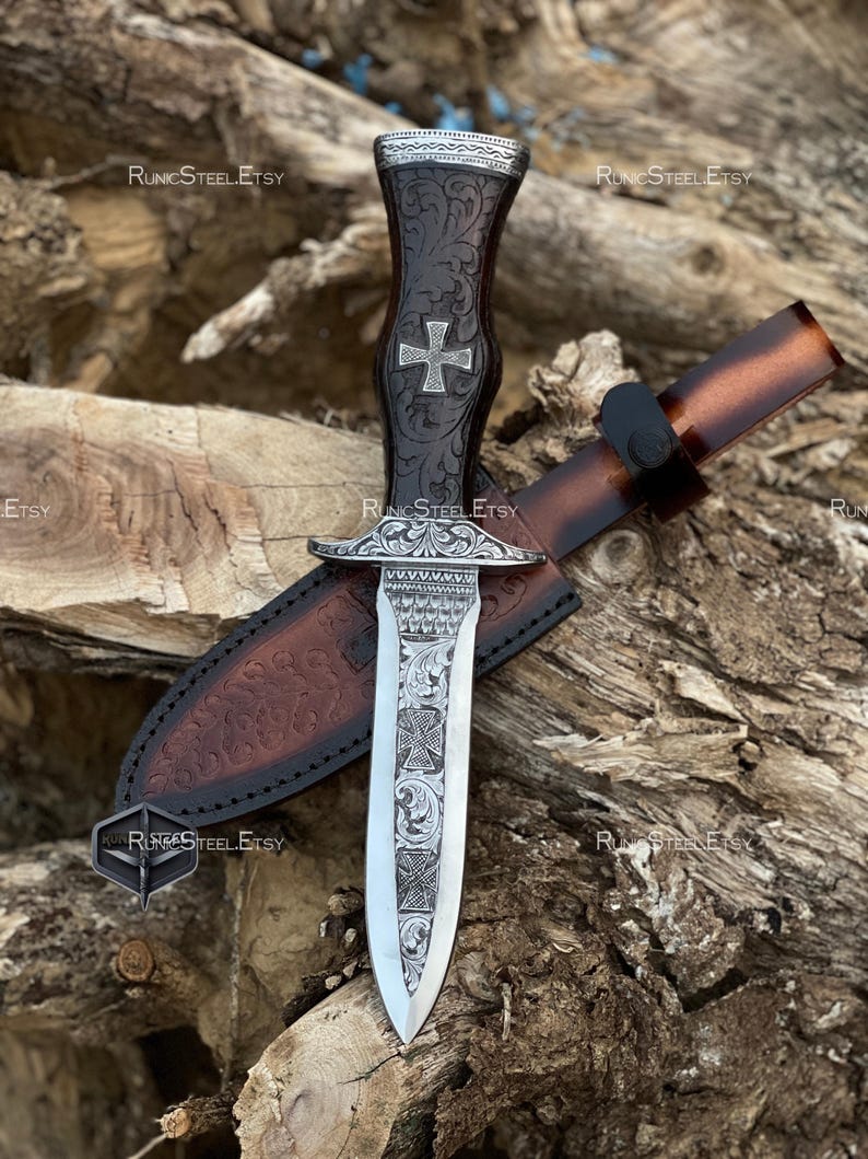 Peut inclure: Un poignard d&eacute;coratif avec une lame argent&eacute;e et un manche marron fonc&eacute; orn&eacute; d'une croix. Le poignard est pr&eacute;sent&eacute; avec un fourreau en cuir marron. Le manche et la lame sont finement grav&eacute;s. Le nom de la boutique Etsy "RunicSteelEtsy" est visible.