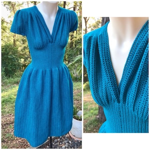 Könnte beinhalten: Türkisfarbenes Kleid mit kurzen Ärmeln und V-Ausschnitt. Das Kleid hat ein figurbetontes Oberteil und einen ausgestellten Rock. Der Stoff scheint ein strukturierter Strick oder Häkelstoff zu sein, mit einer definierten Taille. Das Kleid wird auf einer Schaufensterpuppe präsentiert.