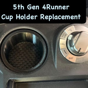 May include: Black cup holder replacement for a 5th Gen 4Runner. The cup holder is round with a textured bottom. The image also shows the 4-wheel drive control knob and the text "5th Gen 4Runner Cup Holder Replacement."