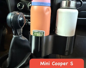 May include: Black double cup holder insert for a Mini Cooper S, designed to fit large bottles. The image shows two water bottles, one orange and pink, the other white, inside the holder. The text on the image reads "Mini Cooper S Double Cup Holder Insert Fits Large Bottles."