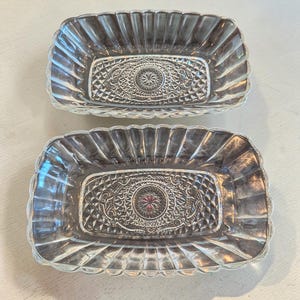May include: Two rectangular clear glass dishes featuring a scalloped rim and a decorative pressed pattern on the base. The centre of each dish displays a circular motif with a small red accent, surrounded by intricate geometric and floral details.