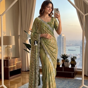 May include: A light green sari with silver detailing and a matching blouse. The sari has an intricate border and is draped gracefully. The fabric displays a delicate pattern, creating a sophisticated and stylish appearance.