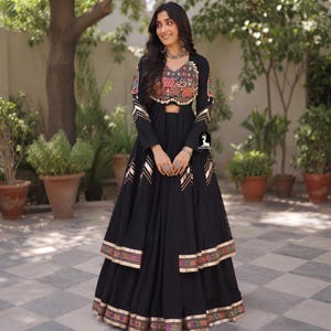 May include: A black long-sleeved floor-length dress featuring a multi-colored embroidered bodice with small hanging beads. The sleeves and hem are accented with gold chevron patterns and a multi-colored geometric border trim at the bottom edge.