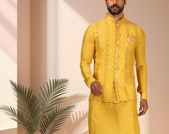Op de afbeelding: Een gele kurta-pyjama set met een bijpassend vest. Het vest heeft een gedetailleerd patroon en is dichtgeknoopt. De outfit wordt gedragen met witte schoenen. De afbeelding bevat een plant in een pot en de tekst "BOLD BOUTIQUE".
