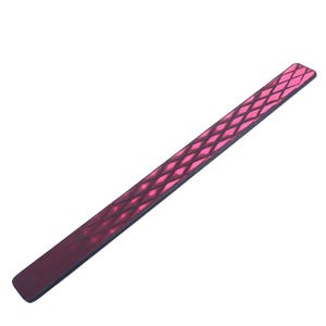 Op de afbeelding: Een lange, smalle, rechthoekige polsband met een levendig roze ruitvormig roosterpatroon tegen een donkerrode achtergrond. De band heeft afgeronde hoeken en een glad, plat oppervlak met een herhalend geometrisch ontwerp.
