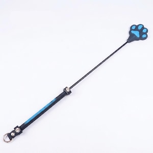 Op de afbeelding: Een zwarte rijzweep met een handvat met blauwe accenten, twee zilverkleurige metalen klinknagels en een zilverkleurige metalen ring aan de basis. Het uiteinde van de zweep heeft de vorm van een pootafdruk met een felblauw midden en een zwarte rand.