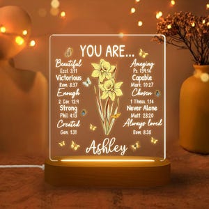 May include: A lighted acrylic plaque with the words "YOU ARE..." and inspirational affirmations, including "Beautiful," "Victorious," and "Always loved." The design features yellow daffodils and butterflies, with the name "Ashley" at the bottom.
