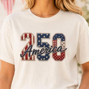 May include: Cream-colored t-shirt featuring the text "250 America" in a patriotic design. The numbers and text are in red, white, and blue, with a stitched effect. The shirt is short-sleeved and has a crew neck.