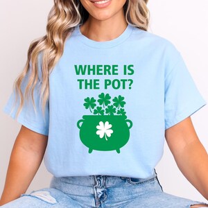 May include: Light blue t-shirt with the text "WHERE IS THE POT?" in green. A green pot of gold with shamrocks is printed on the front. The shirt is a casual style.