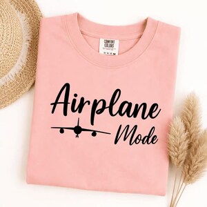 Peachy Comfort Colors tee folded with black Airplane Mode text and airplane icon, stylish travel shirt for vacation wear.