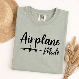 Bay Comfort Colors tee folded with black Airplane Mode text and airplane icon, stylish travel shirt for vacation wear.