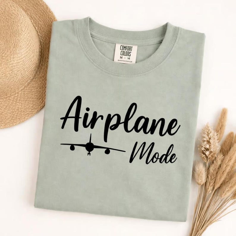 Bay Comfort Colors tee folded with black Airplane Mode text and airplane icon, stylish travel shirt for vacation wear.