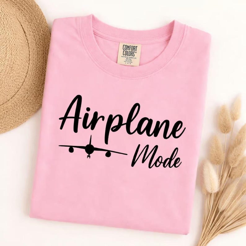 Blossom Comfort Colors tee folded with black Airplane Mode text and airplane icon, stylish travel shirt for vacation wear.