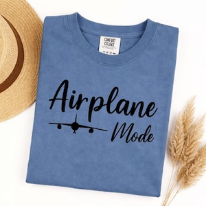 Blue Jean Comfort Colors tee folded with black Airplane Mode text and airplane icon, stylish travel shirt for vacation wear.