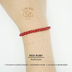 Puede incluir: Una pulsera de rubíes rojos compuesta por pequeñas cuentas redondas. La pulsera se lleva en la muñeca, con el texto "RED RUBY" y texto tailandés debajo. La imagen también presenta un logotipo y texto en tailandés.
