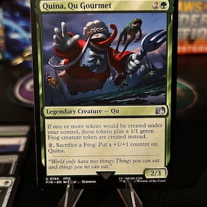 May include: A Magic: The Gathering card featuring Quina, Qu Gourmet. The artwork depicts a red and white creature holding a fork, with a frog on its head. The card has green borders and text that describes the creature's abilities.