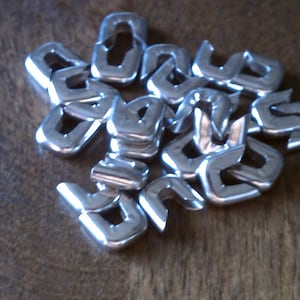 Könnte beinhalten: Ein Haufen silberner Metallverschlüsse oder -befestigungen. Die Verschlüsse sind C-förmig und dazu bestimmt, Stoff oder andere Materialien miteinander zu verbinden.