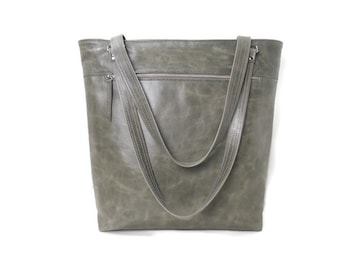 May include: A large, olive green tote bag with two long shoulder straps. The bag has a zippered top and a front zippered pocket. The leather-like material has a distressed appearance. The bag is designed for carrying items.