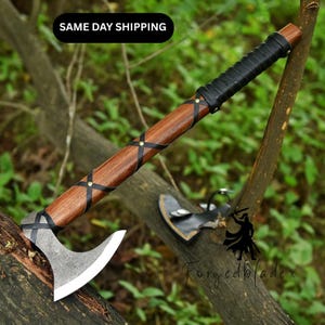 Könnte beinhalten: Eine handgefertigte Axt mit einem Holzgriff, der mit schwarzem Leder umwickelt ist. Der Axtkopf ist silberfarben mit einer scharfen Klinge. Schwarze Lederriemen sind um den Holzgriff gewickelt. Der Text "SAME DAY SHIPPING" befindet sich in der oberen linken Ecke.