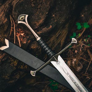 May include: A silver sword with a black handle and sheath lies on a dark, textured surface. The blade has a star design and etched text. The hilt features gold accents.