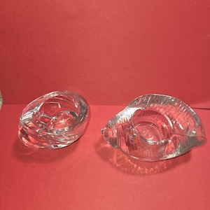 Peut inclure: Deux bougeoirs en verre transparent en forme de coquillages. L'un est en forme de spirale et l'autre en forme de coquillage. Les bougeoirs sont sur un fond rouge. Ces pièces décoratives ajoutent une touche côtière à n'importe quelle pièce.