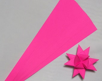 May include: A stack of bright pink origami paper, with a folded pink origami star in the foreground.