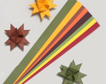 May include: A set of ten paper strips in various shades of brown, yellow, green, and red. The strips are arranged in a fan shape, with the darkest shade at the bottom and the lightest shade at the top. Three origami stars are also shown in the image, one yellow, one brown, and one green.