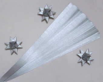 Puede incluir: Una manualidad de papel gris claro en forma de abanico con tres adornos en forma de estrella. El abanico está hecho de muchas tiras de papel finas y paralelas. Los adornos de estrella están hechos de papel plegado.