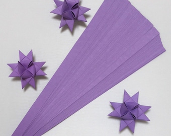 May include: A pack of 50 lavender origami paper strips. The strips are arranged in a fan shape. Three origami stars made from the paper are also shown.