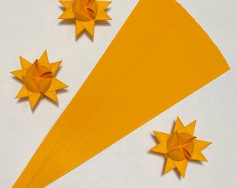 May include: A pack of 25 bright yellow paper strips for making origami stars. The strips are arranged in a fan shape and three finished origami stars are shown.