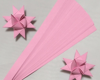 May include: A stack of pink origami paper strips, with two finished pink origami stars. The paper strips are about 1/2 inch wide and 11 inches long.