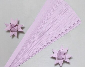 May include: A stack of 50 lavender paper strips for origami. The strips are arranged in a fan shape. Two finished origami stars are also shown.