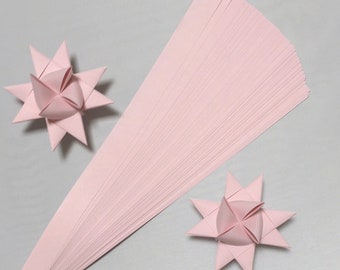 May include: A stack of pink paper strips for making origami stars. Two finished origami stars are shown on a white background.