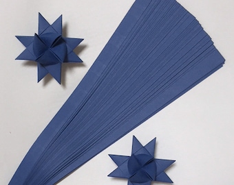 May include: A stack of 50 blue paper strips for making origami stars. The strips are 1/2 inch wide and 12 inches long. Two finished origami stars are shown in the image.