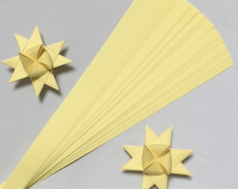 May include: A pack of 25 yellow paper strips for making origami stars. The strips are arranged in a fan shape. Two finished origami stars are also shown.