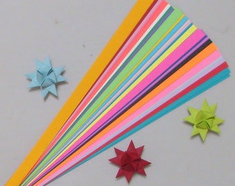 May include: A stack of colorful origami paper strips in various shades of yellow, orange, red, pink, purple, blue, green, and white. The paper is arranged in a fan shape, with the yellow strip at the top and the white strip at the bottom. There are three origami stars made from the paper, one blue, one green, and one red.