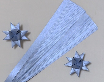 Puede incluir: Una pila de tiras de papel azul claro para origami, con dos estrellas de origami terminadas hechas del mismo papel.