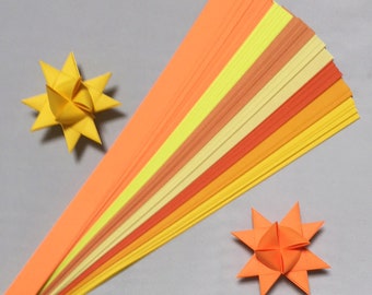 May include: A set of 15 orange, yellow, and peach colored paper strips for origami. The strips are arranged in a fan shape. Two origami stars are also shown, one yellow and one orange.