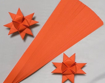 May include: A bundle of orange paper strips for making origami stars. Two finished origami stars are shown on a white background.
