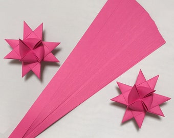 May include: A pack of pink paper strips for making origami stars. The pack contains multiple strips of paper, and there are two finished origami stars in the image.