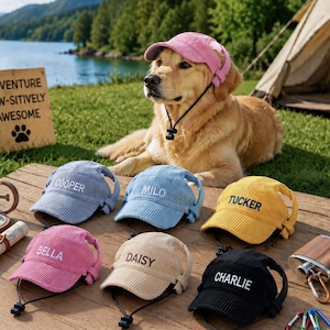 Könnte beinhalten: Sechs Kord-Mützen für Haustiere in Hellblau, Mittelblau, Gelb, Pink, Beige und Schwarz, jeweils mit eingesticktem Namen und verstellbarem Kinnriemen. Ein Golden Retriever trägt eine passende pinke Mütze neben einem hölzernen Schild.